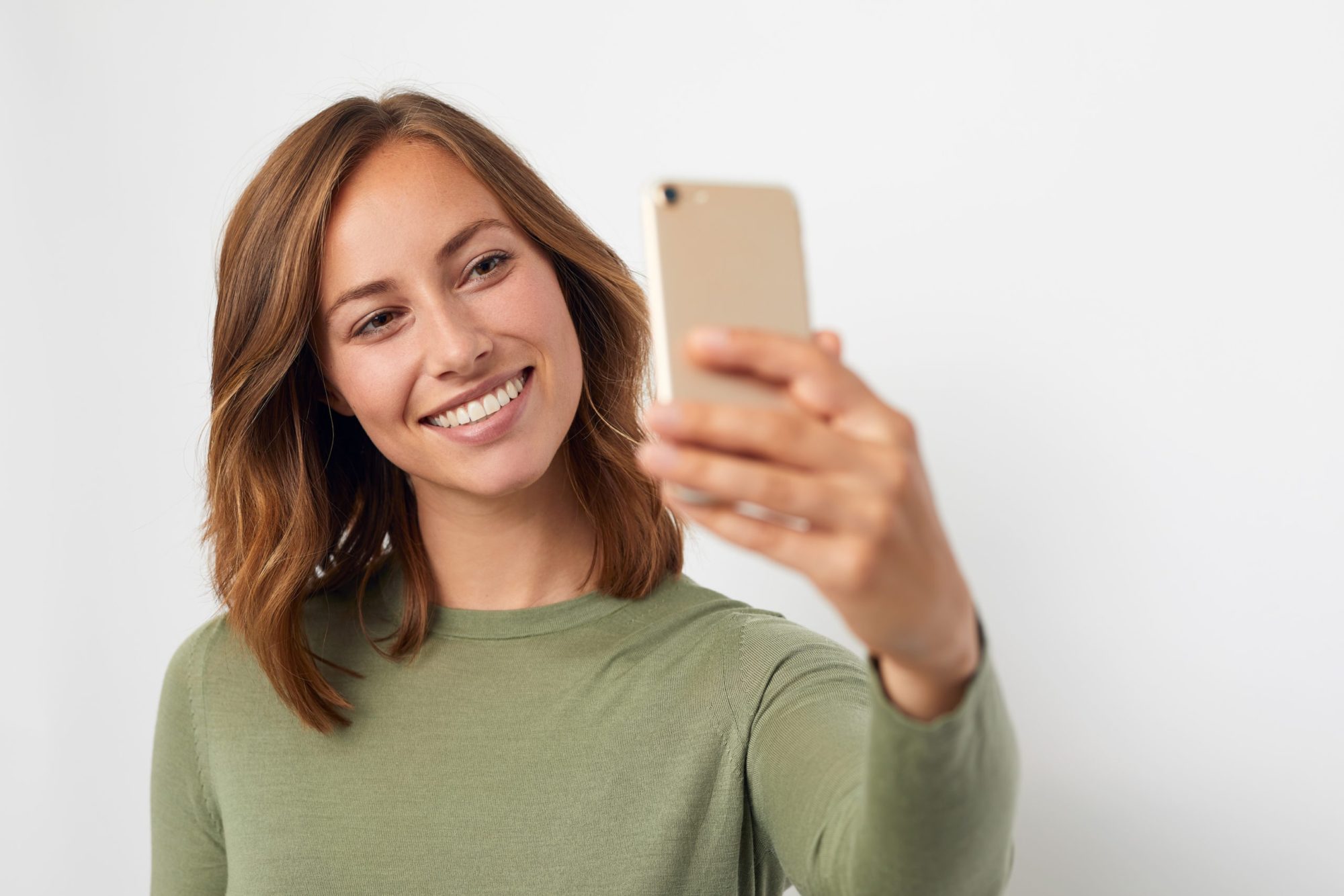 Smiling woman in a green top taking a selfie, showing the camera-ready confidence that adults and teens can get from Invisalign treatment with Dr. Ryan Hecht at Montana Smiles Orthodontics in Billings, MT.